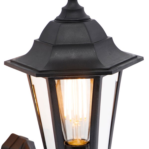 Detailansicht einer schwarzen Außenwandleuchte im Laternen-Stil mit klarem Glas und leuchtendem Filament-Leuchtmittel.