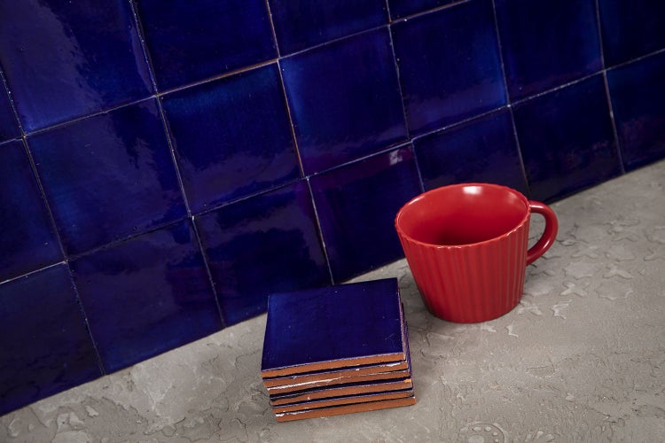 Quadratische, glänzende Fliesen an der Wand, Fliesenstapel und eine Tasse.