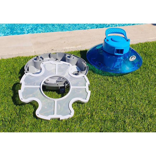 Zerlegter Poolreiniger aus Kunststoff mit blauem Gehäuse, grauem Bodenteil und weißem Filternetz auf einer Rasenfläche an einem hellen Beckenrand.