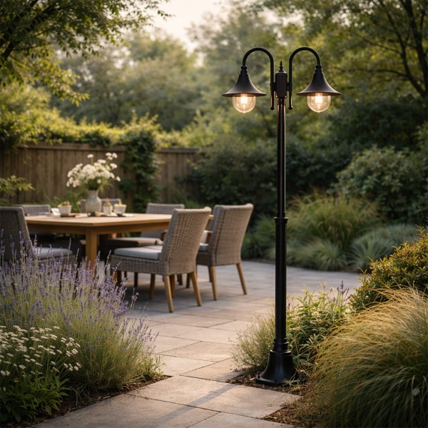 Zweiflammige Gartenlaterne aus Metall mit zwei Lichtquellen auf einer Terrasse mit Sitzgruppe im Hintergrund.