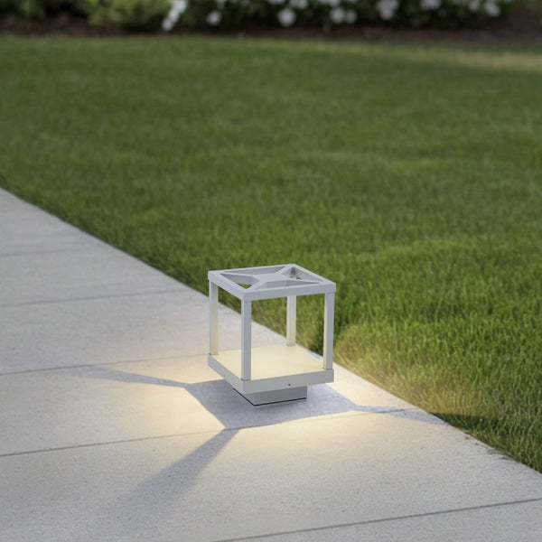 Moderne quadratische Außenleuchte mit offenem Rahmen platziert auf einem Gartenweg neben einer Rasenfläche.