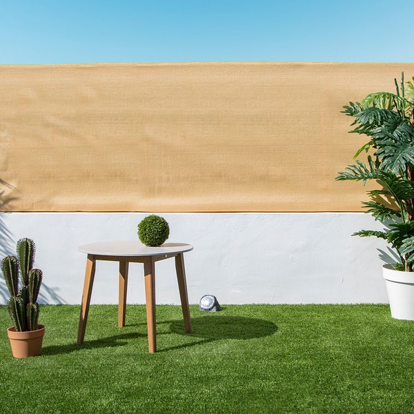 Balkonsichtschutz in Sandfarben auf einer Terrasse mit Kunstrasen, rundem Holztisch und Topfpflanzen.