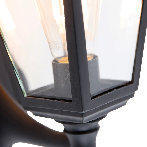 Nahaufnahme einer schwarzen Außenwandleuchte im Laternen-Stil aus Metall und Klarglas mit einem Edison-Leuchtmittel.