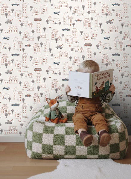 Kind liest Buch auf einem Sitzsack vor einer Wandtapete mit Stadtmotiven