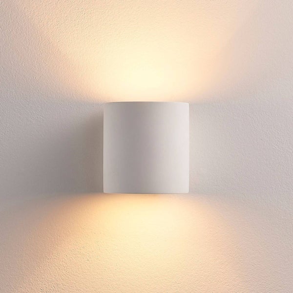 Weiße zylindrische Wandleuchte mit Up and Down Lichteffekt, wirft warmes Licht nach oben und unten an eine Wand.