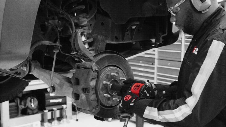 Ein Mechaniker benutzt einen Schlagschrauber, um an einem Auto zu arbeiten.