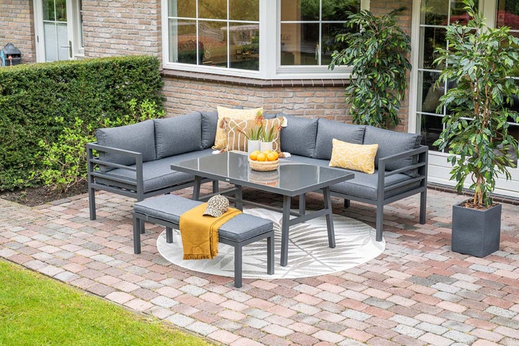 Modernes L-förmiges Garten-Lounge-Set aus grauem Metall mit passendem Tisch und Bank auf einer gepflasterten Terrasse.
