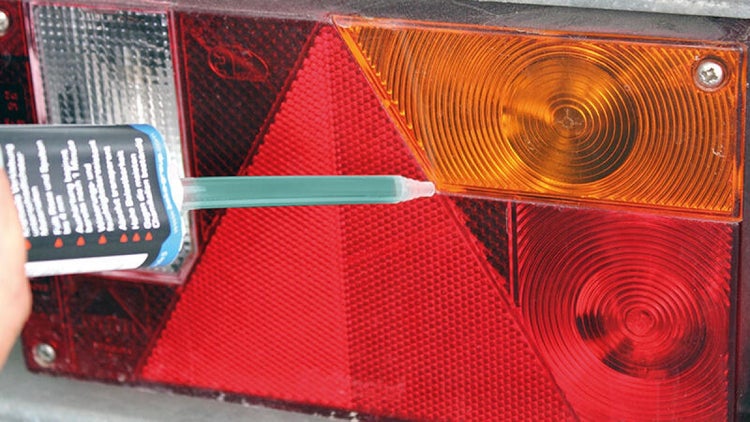 Auftragen von Klebstoff auf eine Fahrzeugleuchte mit rotem Reflektor, gelbem Blinker und weißem Rückfahrlicht