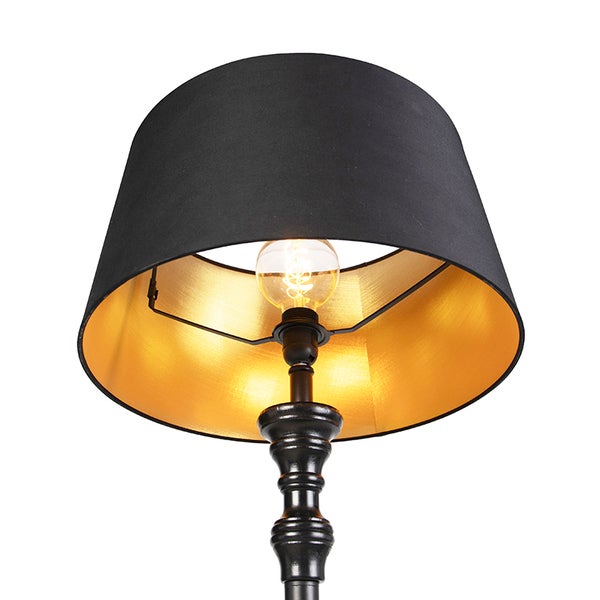 Lampe mit schwarzem Stoffschirm, goldener Innenseite, dekorativem schwarzem Metallständer und leuchtender Filament-Glühbirne.
