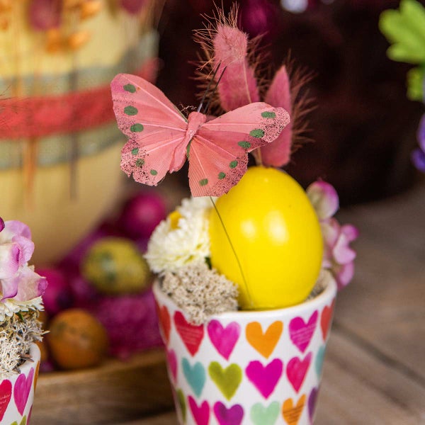 Dekoration mit gelbem Osterei, rosa Schmetterling und Topf mit Herzmuster