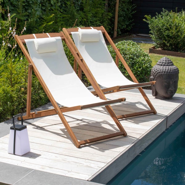 Zwei Gartenliegen aus Holz mit hellen Stoffbezügen und Kopfkissen auf einer Holzterrasse am Pool im Garten.
