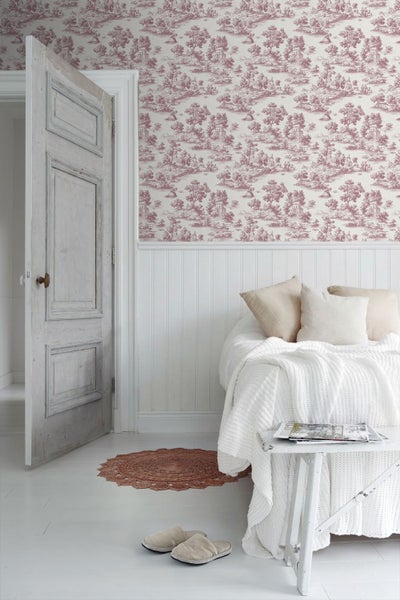Hell gestalteter Raum mit Toile-de-Jouy-Mustertapete, halbhoher Holzvertäfelung, einer rustikalen Holztür und einem Bett mit strukturierten Textilien.