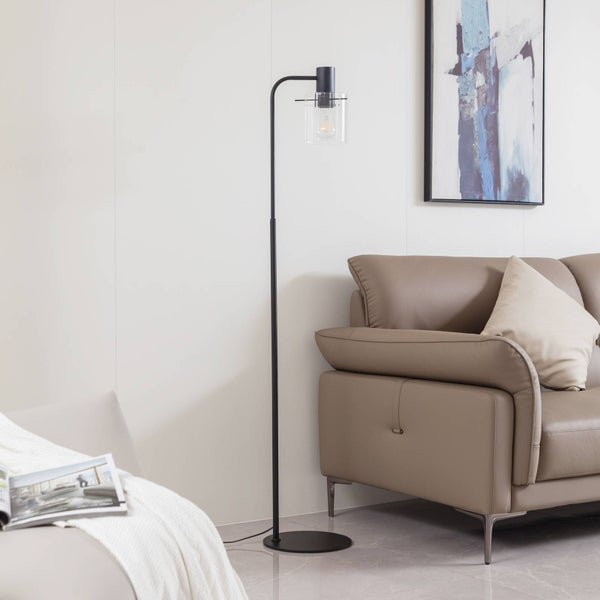 Schwarze Stehlampe mit klarem Glasschirm neben beigem Sofa