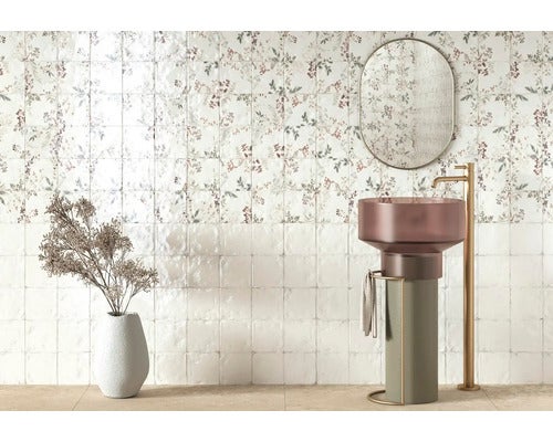 Wandfliesen mit floralem Muster und glänzende Fliesen im Badezimmer mit freistehendem Waschbecken, Armatur und Spiegel.