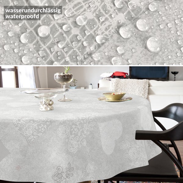 Runde, wasserabweisende Tischdecke mit hellgrauem Spitzenmuster aus Herzen und Blumen, Detailaufnahme mit Wassertropfen.