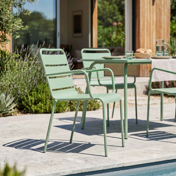 Moderner Gartenstuhl aus Metall mit Armlehnen und Lamellen-Design auf einer hellen Terrasse neben einem Gartentisch.