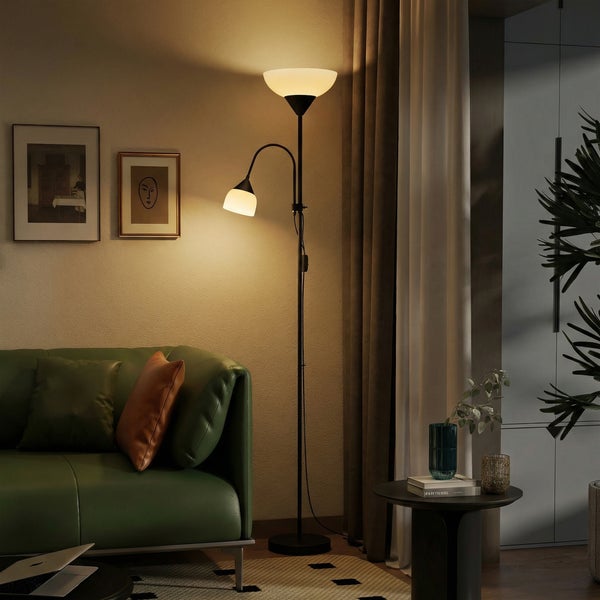 Moderne Stehleuchte mit Deckenfluter und verstellbarem Lesearm in einem gemütlich eingerichteten Wohnzimmer neben einem grünen Sofa.
