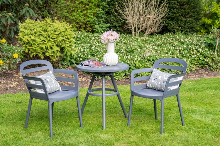 Modernes Gartenmöbel-Set mit zwei grauen Sesseln aus Kunststoff und einem runden Tisch auf einer Rasenfläche vor üppigem Grün.