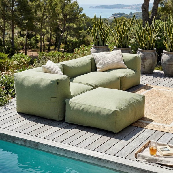 Modulares Garten-Loungesofa mit Hocker auf einer Holzterrasse am Pool mit Pflanzen im Hintergrund.