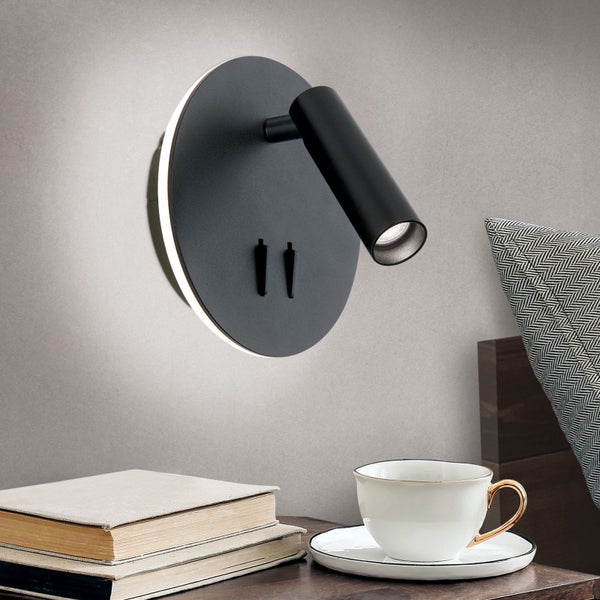 Schlafzimmer-Szene mit einer schwarzen LED-Wandleuchte über einem Nachttisch mit Büchern und einer Teetasse