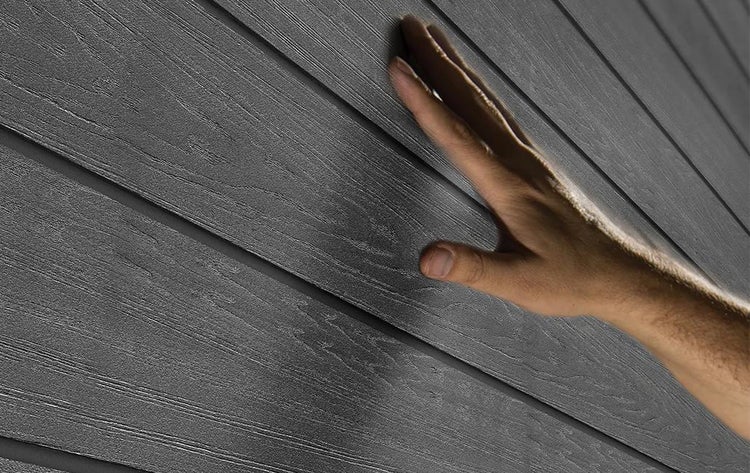 Hand berührt die strukturierte Oberfläche von Fassadenpaneelen mit Holzmaserung.