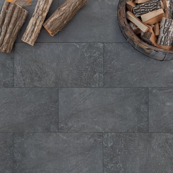 Dunkelgraue Bodenfliesen in Steinoptik, verlegt im Versatz neben Kaminholz.