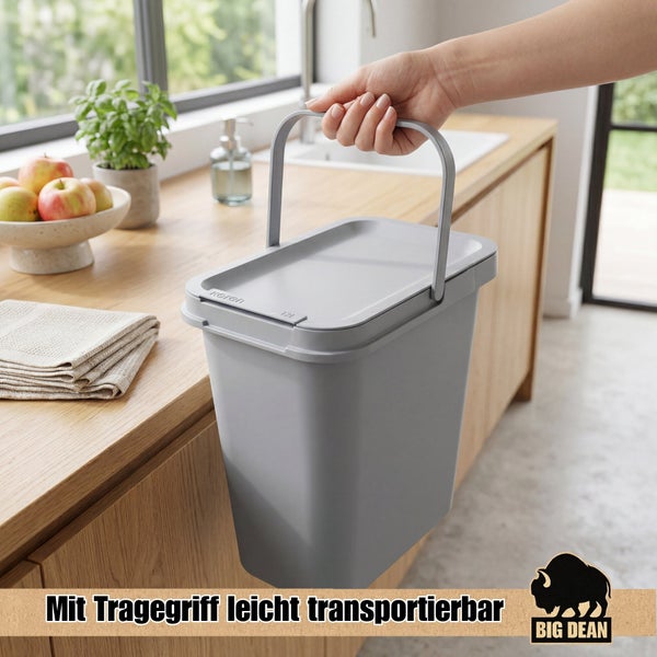 Ein grauer Kunststoffmülleimer mit Tragegriff und Deckel wird in einer Küche gehalten.