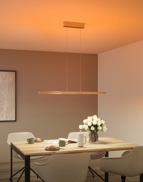 Moderne, schmale LED-Pendelleuchte über einem hölzernen Esstisch mit Blumen und Geschirr in einem warm beleuchteten, minimalistischen Raum.