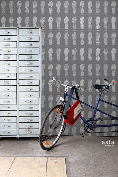 Raumszene mit einer Schubladenkommode, einem Fahrrad und einer Tapete mit Fußabdruckmuster