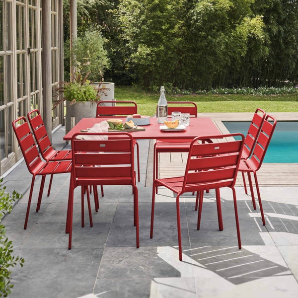 Gartenset aus rotem Metall mit rechteckigem Tisch und sechs Stühlen mit Lamellen auf einer Terrasse neben einem Pool im Garten.