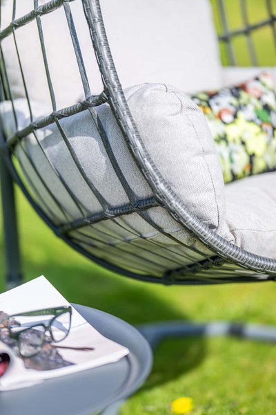 Nahaufnahme eines Hängesessels aus Polyrattan-Geflecht mit Polstern im Garten.