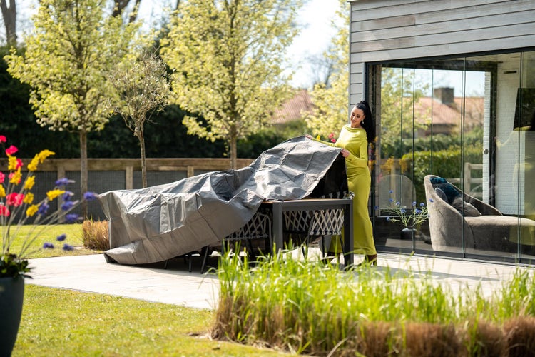 Gartenszene mit einer Frau, die eine graue Schutzhülle über eine Gartengarnitur legt
