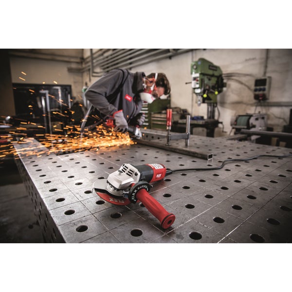 Winkelschleifer von Flex auf einem Werkstatttisch bei der Metallbearbeitung, während im Hintergrund ein Arbeiter Funken beim Schleifen erzeugt