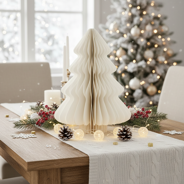 Festlich dekorierter Holztisch mit weißem Tannenbaum aus plissiertem Papier, Tannenzweigen, Zapfen und einer Lichterkette.