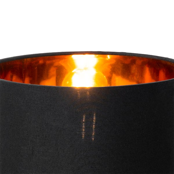 Schwarzer Lampenschirm aus Stoff mit goldener Innenseite und eingeschaltetem Leuchtmittel.