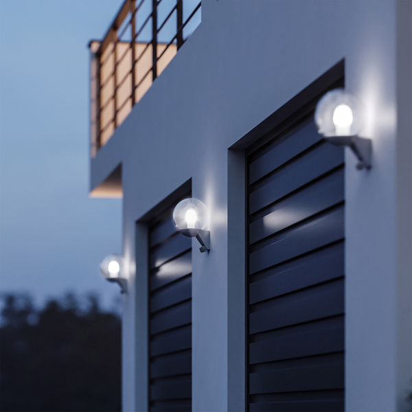 Kugelförmige Außenwandleuchten aus Glas an einer weißen Hauswand neben dunklen Lamellen bei Dämmerung.