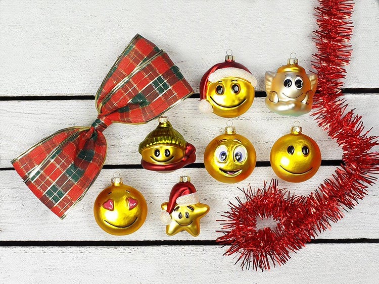Set mit sieben verschiedenen weihnachtlichen Smiley Christbaumkugeln aus Glas mit roter Schleife und Lametta auf einem hölzernen Untergrund