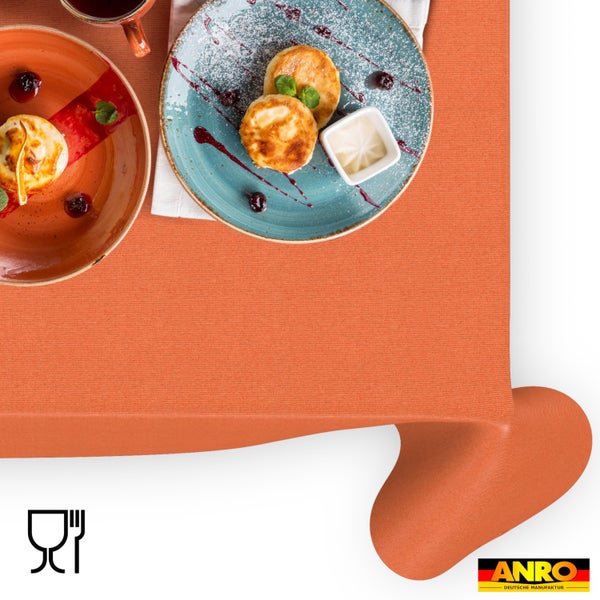 Hell gedeckter Tisch mit orangefarbener, strukturierter Tischdecke, Tellern mit Speisen und Beeren. ANRO Logo und Symbol für Lebensmittelechtheit.