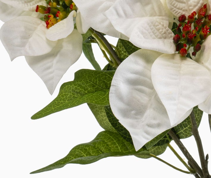 Nahaufnahme eines künstlichen Weihnachtssterns mit weißen Hochblättern, grünen Blättern und roten Details in der Mitte.