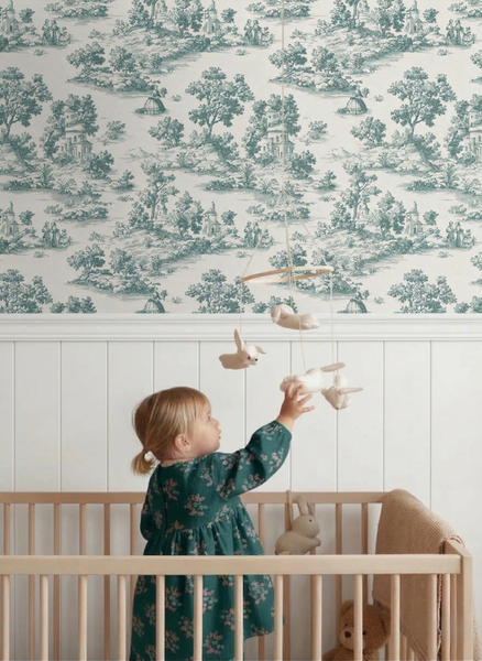Helles Kinderzimmer mit Toile-de-Jouy-Tapete, weißer Wandvertäfelung aus Holz und einem Babybett aus hellem Holz.