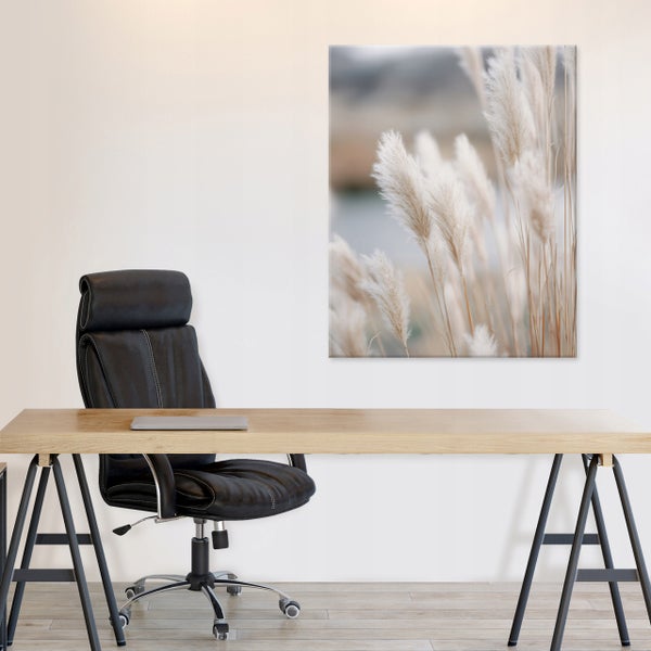 Ein moderner Schreibtisch mit schwarzem Bürostuhl und einem Wandbild mit Gräsermotiv in einem hellen Arbeitszimmer.