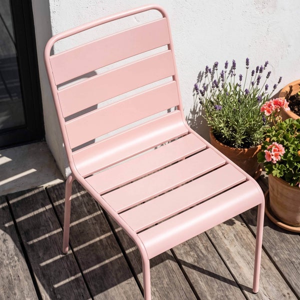 Moderner rosa Gartenstuhl aus Metall mit Latten auf einer hellen Holzterrasse neben Blumentöpfen.