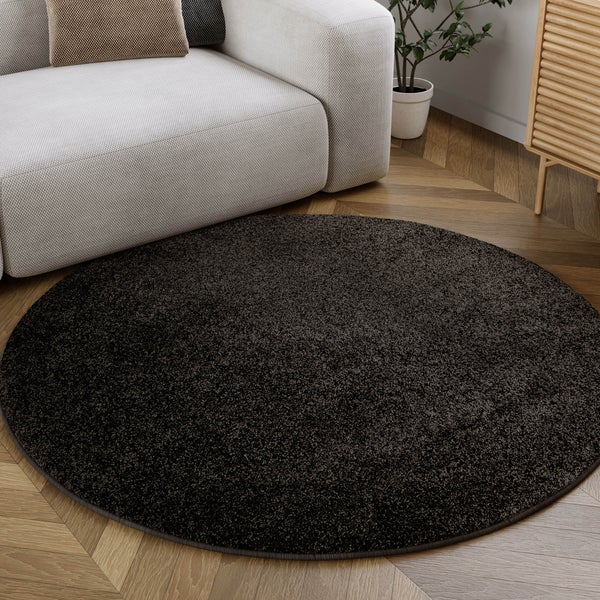 Runder dunkelbraun melierter Teppich auf hellem Fischgrät-Parkett im Wohnzimmer neben einem hellgrauen Sofa.