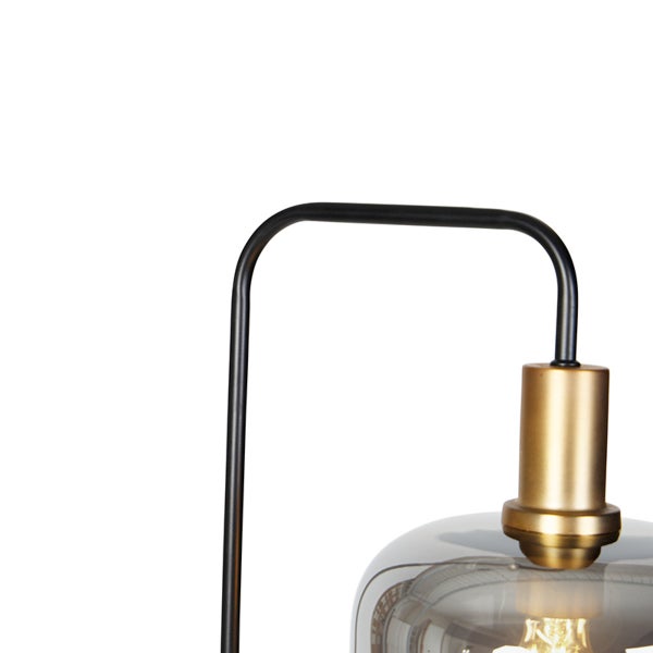 Nahaufnahme einer modernen Leuchte mit schwarzem Metallgestell, goldfarbener Fassung und rauchgrauem Glasschirm.