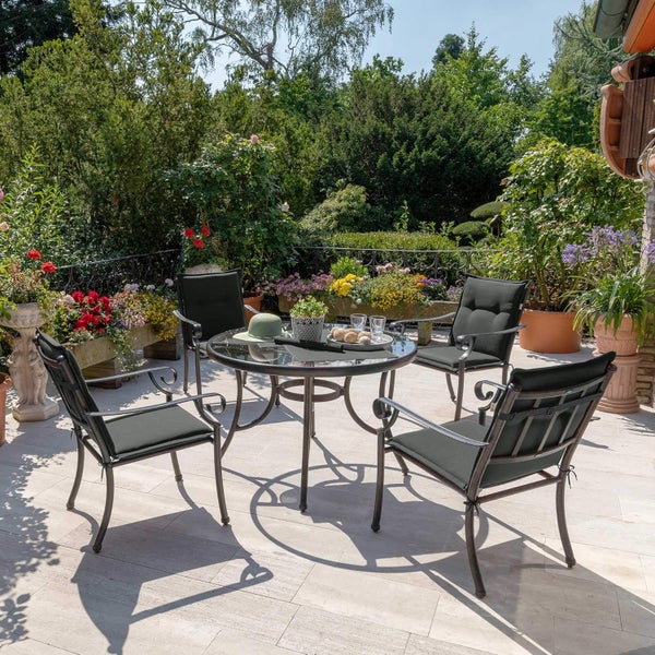 Helle Terrasse mit Gartenmöbelset bestehend aus rundem Glastisch und vier Sesseln mit Auflagen, umgeben von Pflanzen und Blumen.