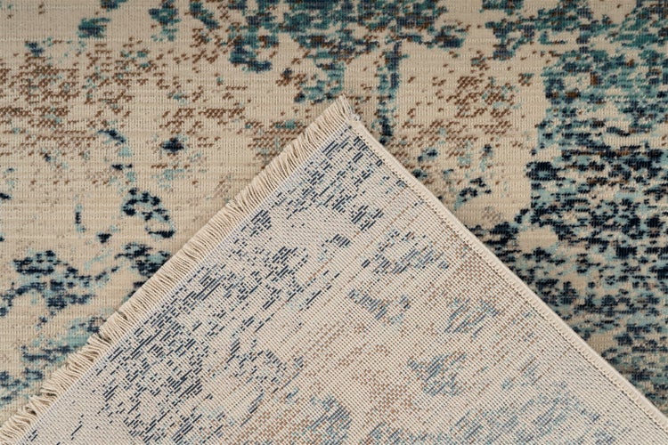 Teppich mit abstraktem Muster, umgeknickte Ecke zeigt die gewebte Rückseite und Fransen.