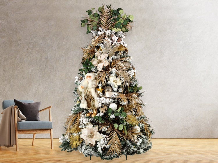 Festlich geschmückter, künstlicher Weihnachtsbaum mit Schneeoptik, goldenen Dekoelementen, Blumen und einer Weihnachtsmannfigur im Wohnzimmer.