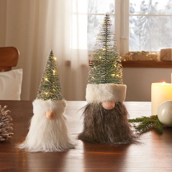 Zwei dekorative Weihnachtszwerge mit Bart und beleuchtetem Tannenbaum auf einem Tisch.