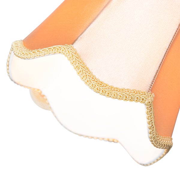 Detail eines orangefarbenen Lampenschirms aus Stoff mit gewelltem Rand und goldener Zierborte.
