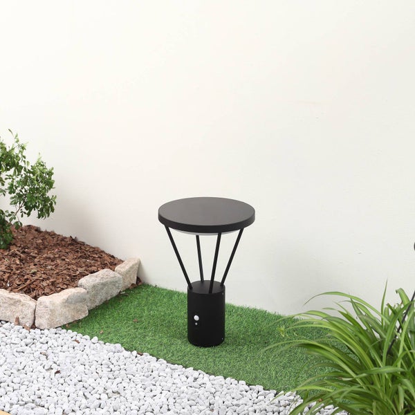 Moderne schwarze Wegeleuchte mit Bewegungsmelder in einem Garten mit Kunstrasen, weißen Kieselsteinen und Pflanzen.